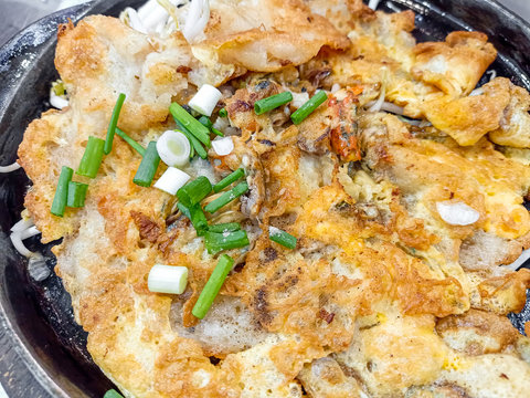 Crispy fried oyster pancake in hot plate . Oyster omelette or Fried clams . Thai food in hot pan with crispy flour and egg Popular manu Thai Cuisine. Delicious food on the sidewalk.
