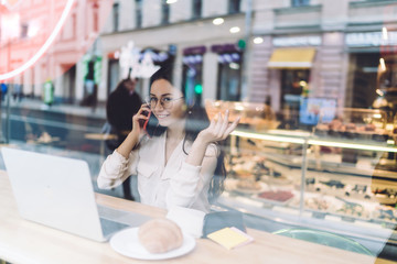 Smiling freelancer speaking on smartphone in cafe