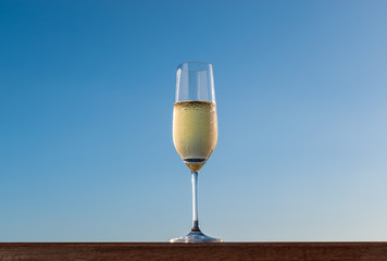 One flute glass with sparkling champagne against blue background. New Year's celebration alcoholic bubbly beverage.