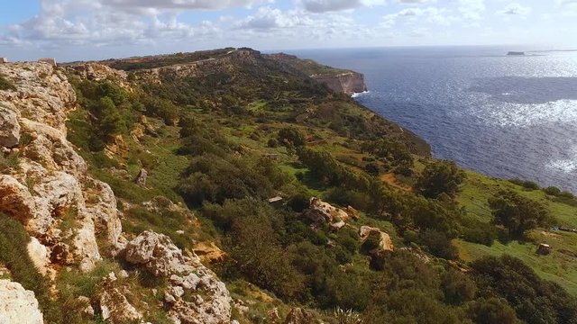 Malta Dingi cliff colourful coastal island landscape scene. Tilt up across coastal vista overlooking ocean coastline seascape.