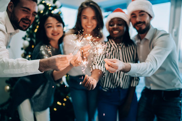 Cheerful group of friends showing sparklers to camera