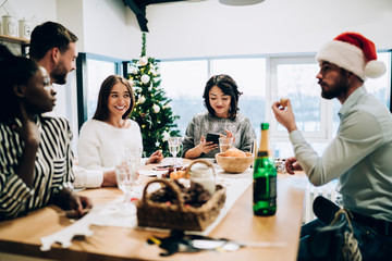 Happy group of friends with woman browsing mobile while celebrating New Year weekend at home