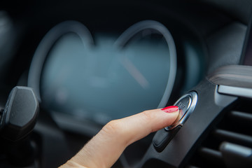 female finger presses the start stop engine button on a car dashboard. close-up, soft focus, in the background the dashboard and car speedometer in blur, side view