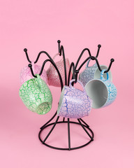 A set of tea mugs hanging on a hanger for mugs on a pink background