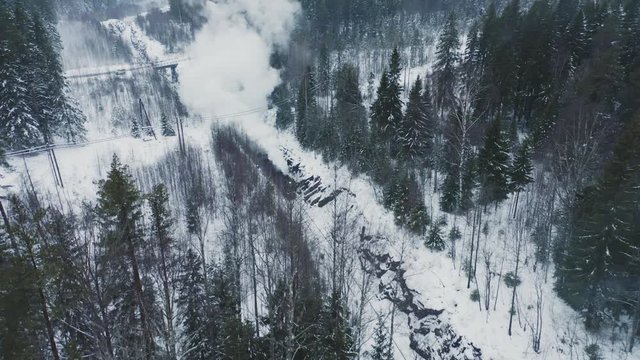 Aerial view retro steam locomotive running in snow covered forest. Winter forest