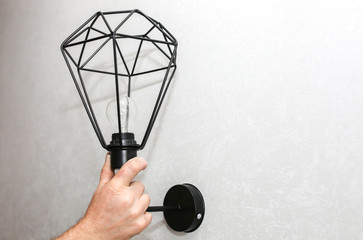 Man holding lamp in hands. Electricity installation. Modern loft design. Restoration indoors. Maintenance work.