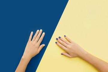 Bright trendy female manicure. Woman's hands with yellow and blue manicure on yellow and blue background.