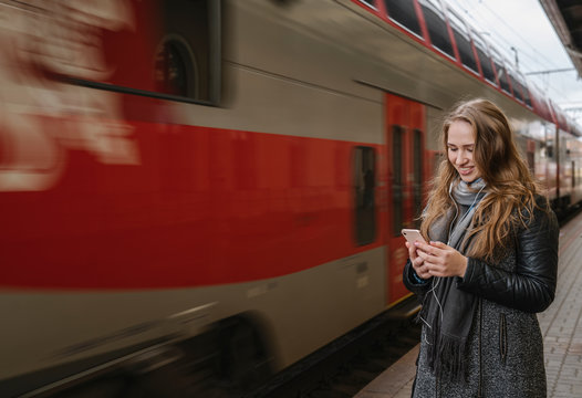Smiling young woman standing on platform using smartphone and earphones, Vilnius, Lithuania