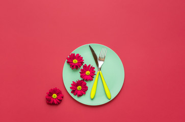 Green plate with cutlery and red flowers. Spring dinner table