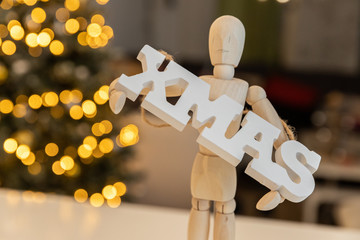 Wooden manikin holding wooden woord xmas, yellow bokhe background 