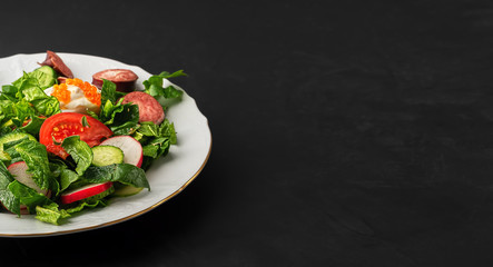 Fresh vegetable salad with tomatoes, radish eggs, caviar and onions. Black background with copy space. Close-up.