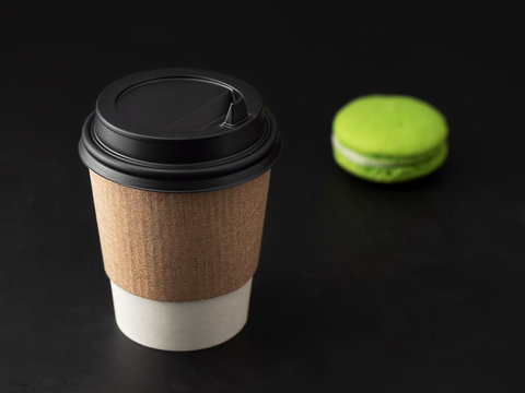 Paper cup with a hot drink, coffee or tea on a black background. Near macaroons. Close-up.