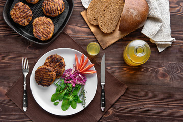 Obraz na płótnie Canvas Top view of country dinner with cutlet and fresh salad, brown bread and moonshine on rustic wooden table