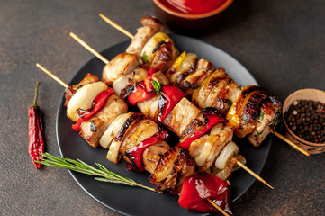 Meat skewers with grilled vegetables on a black plate on a stone background 