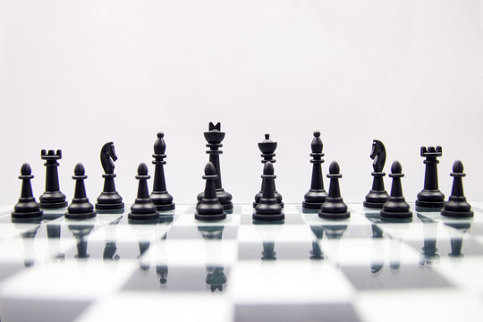black chess pieces stand on a mirror chessboard on a white background