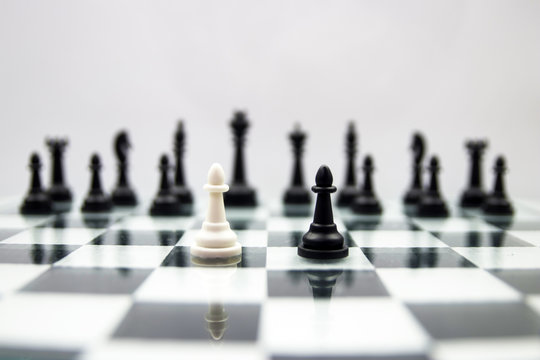 black and white pawns stand on a mirrored chessboard against the background of other black chess pieces