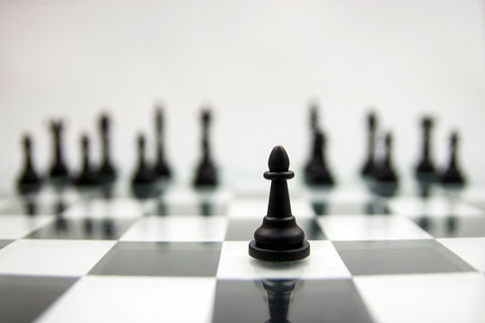 A black pawn stands on a chessboard against the background of blurry remaining pieces.
