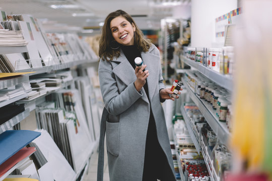 Cheerful artist young pretty woman choosing watercolor at stationery store