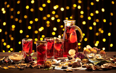 Obraz na płótnie Canvas Christmas mulled wine or gluhwein with spices, chocolate sweets and orange slices on rustic table, traditional drink on winter holiday, christmas lights and decorations