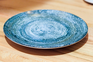 Fototapeta na wymiar Textured plate handmade on a wooden surface. Beautiful blue plate with swirling stripes on a wooden background. Empty bowl on rustic wood, Japanese handmade ceramic bowl, ceramic texture