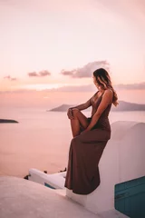 Muurstickers Young woman with blonde hair and purple dress watching the sunset in santorini greece © Mathilda