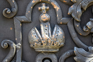 Fragment of a forged metal door with a crown ornament with a cross. Black color. Religious design.  The symbol of power. Close-up. Selective focus.