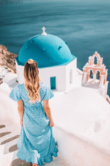 Young woman with blonde hair and blue dress in oia, santorini, greece with ocean view and churches