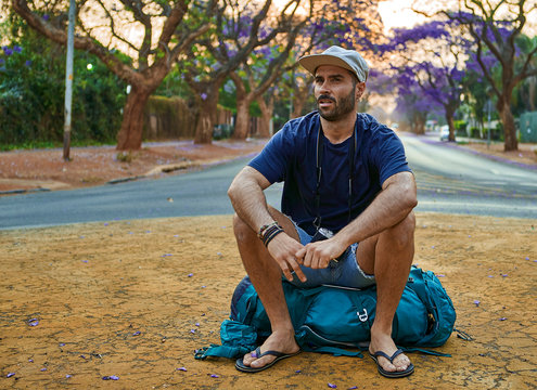 Backpacker sitting on his bag in the middle of a street