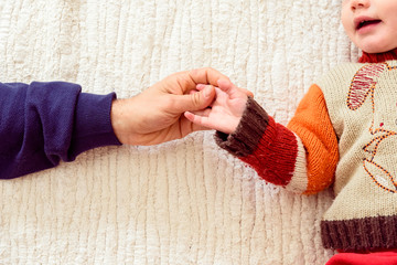 Father shakes hands with his baby daughter lying in bed.