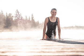 Happy woman wearing black swimsuit bathing in a lake at morning mist