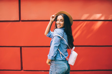 Half length portrait of cheerful Ukrainian woman posing near brick wall enjoying free time for recreating, positive hipster girl in joyful mood laughing near promotional background at urban setting