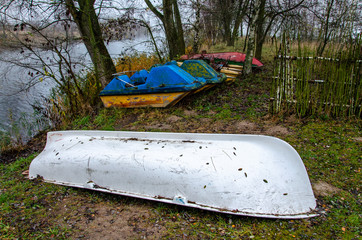Old boats and catamarans are rusting in the open. Dump in the forest at the foot of the river bank...