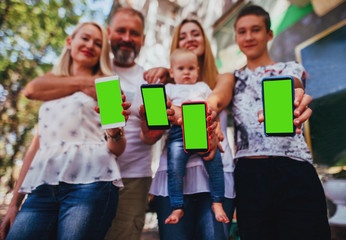 Hands of family members holding mobile smart phones with green screen.