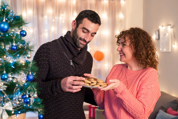 Beautiful brunette in a pink sweater giving Christmas cookies to his boyfriend
