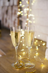 Celebratory glasses with champagne on a New Year's table. Background for christmas or new year with garland and bokeh. A romantic evening.