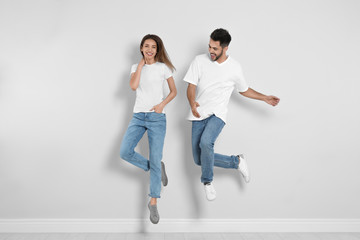 Fototapeta na wymiar Young couple in stylish jeans jumping near light wall