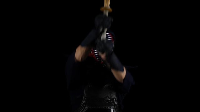 Masculine Kendo warrior practicing martial art with the bamboo bokken on black background. Slow motion