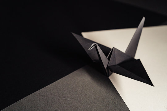 origami crane made of dark gray paper stands on sheets of paper