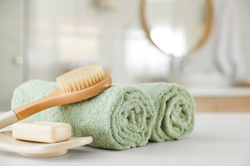 Clean rolled towels, massage brush and bar of soap on table in bathroom - obrazy, fototapety, plakaty