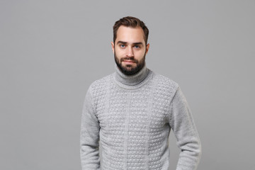 Handsome young bearded man in gray sweater posing isolated on grey wall background, studio portrait. Healthy fashion lifestyle, people emotions cold season concept. Mock up copy space. Looking camera.