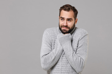 Obraz premium Mrożony młody człowiek w szarym swetrze pozowanie na białym tle na szarym tle, portret. Zdrowy styl życia moda, ludzie emocje koncepcja zimnego sezonu. Makieta miejsca na kopię. Ogrzewające dłonie, patrząc na bok.