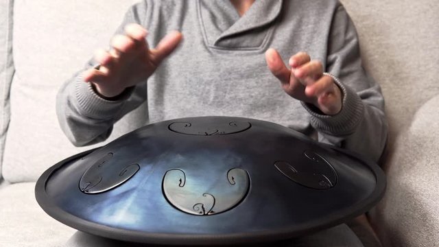Close up of man hands playing hang drum indoors. Unusual music instrument. Concept of sound for meditation