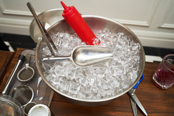 Silver ice bucket with silver ice scoop and ice cubes, close-up.