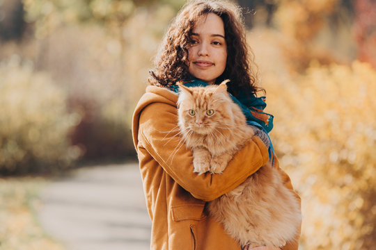 A girl walks with a red cat along the autumn street.