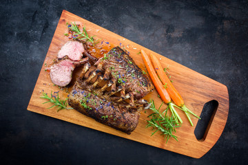 Barbecue rack of lamb with carrot and herbs offered as top view on a modern design wooden board...
