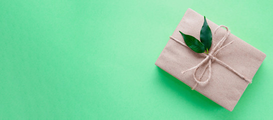 Gift box wrapped in kraft paper tied with twine decorated with two green leaves on neo mint background. Trend color 2020. Banner. DIY. Zero waste holidays concept. Flat lay. Copy space