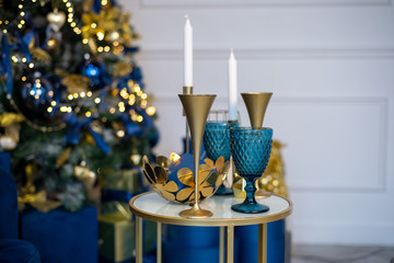Blue glass and gold metallic holiday glasses, New Year's dinner, decor in blue and gold colors against the backdrop of a Christmas tree and lights