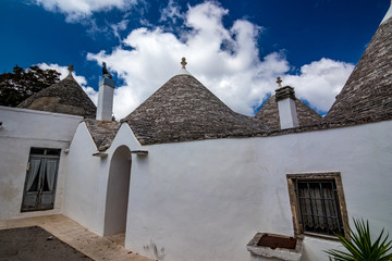 Fototapeta na wymiar Roofs and entrances of truli, typical whitewashed cylindrical houses in Alberobello, Puglia, Italy with amazing blue sky with clouds, street view