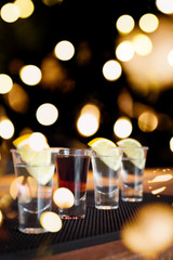 Brandy and three tequila shots with lemon on a bar ribber mat. Shallow DOF and toned with festive bokeh lights