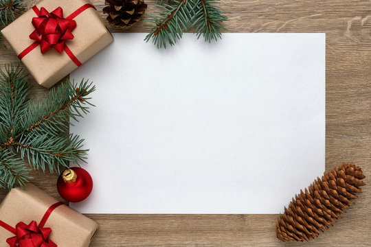 Christmas or New Year background. White sheet of paper with copy space, gift boxes, Christmas balls and Christmas tree branches on wood. Flat lay, top view